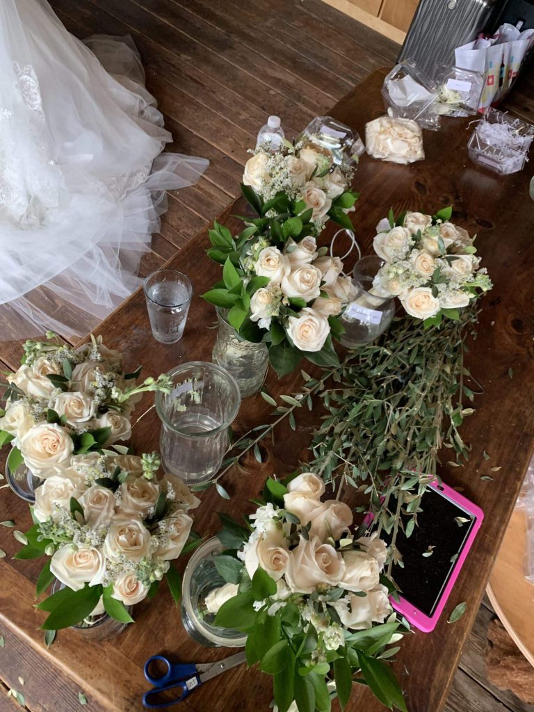 Bouquets of white roses and greenery on the wood table in the bridal backstage area